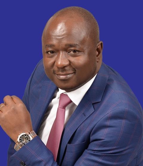 Portrait of Mark Nyamita in a blue suit and pink tie against a blue background