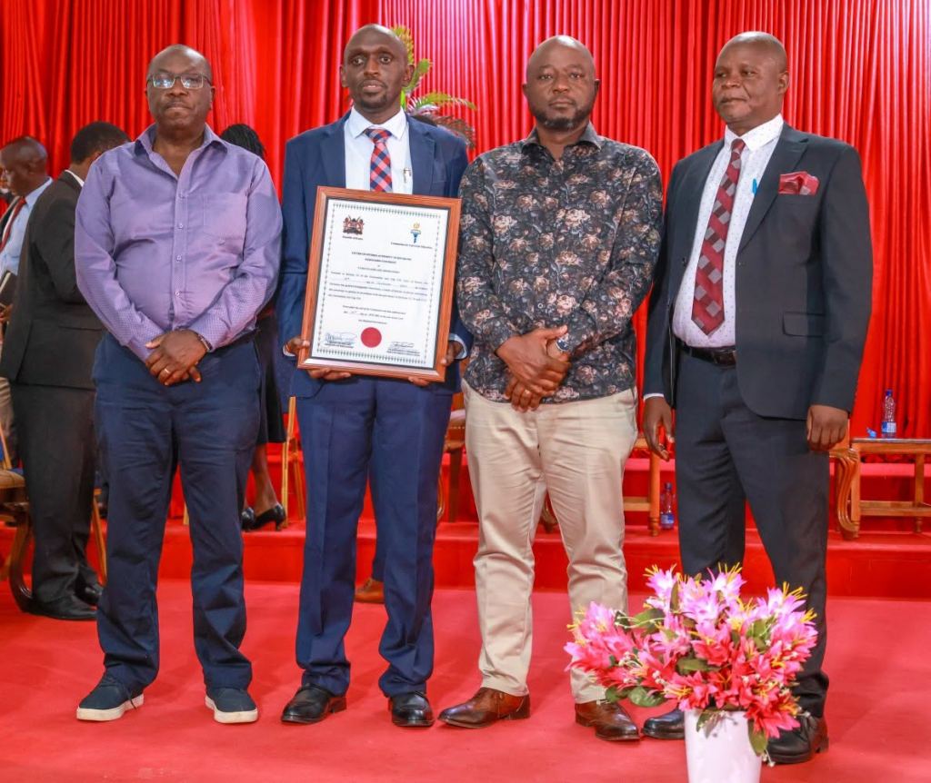 Four men stand together holding a framed certificate at a ceremony