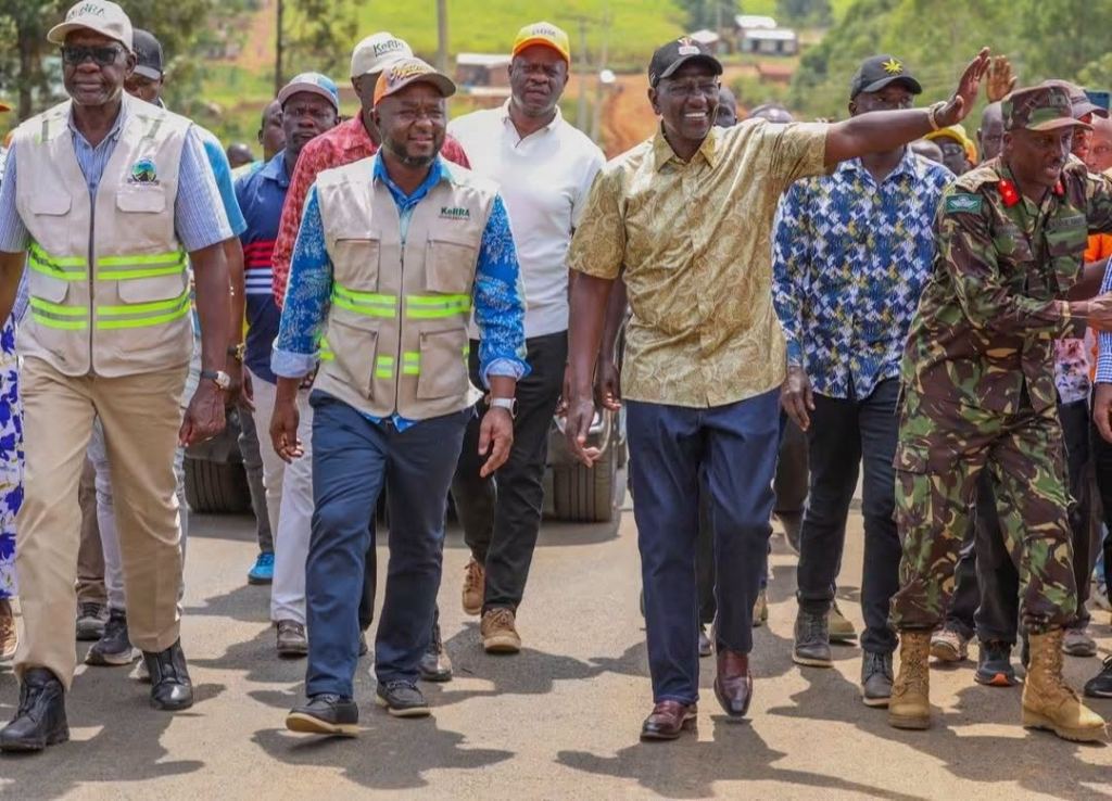 Officials in high-visibility vests walk along a road during a site visit