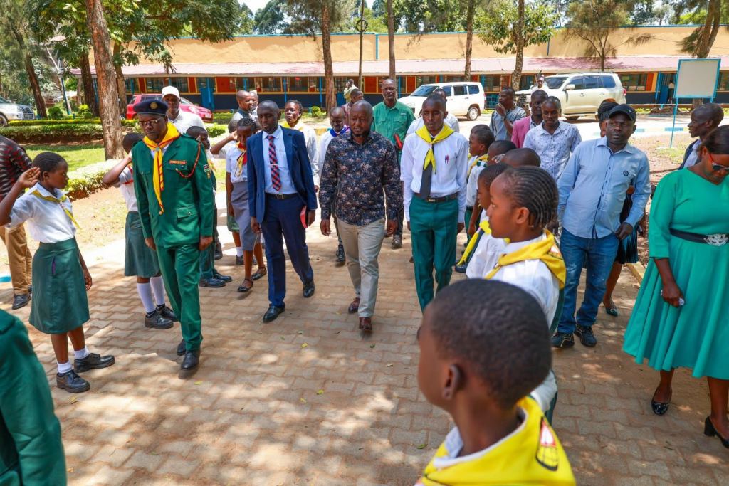 A delegation walks through a school compound as pupils look on